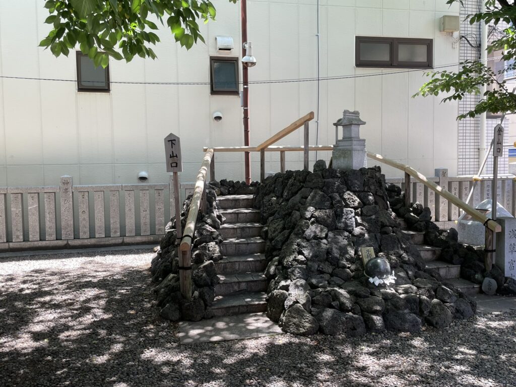 浅草富士浅間神社の富士塚全景。溶岩石が積まれた小山と周囲の緑。