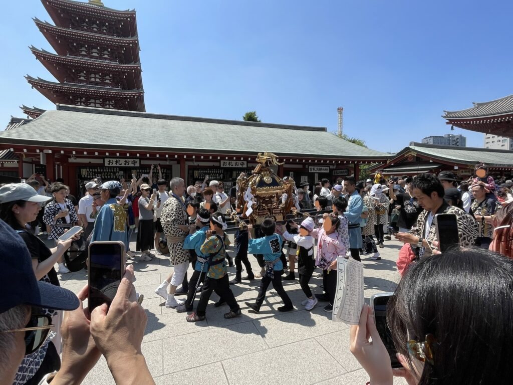浅草寺境内を元気よく進む子供神輿。五重塔を背景に祭りの華やかさが際立つ。