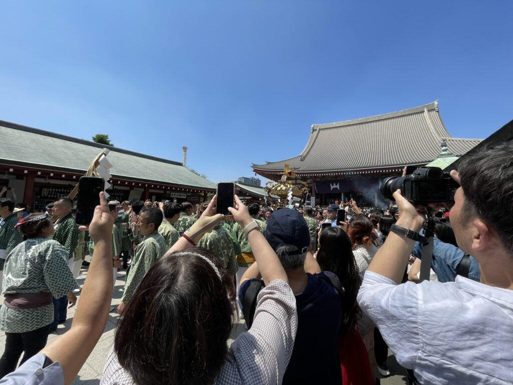 大勢の人がスマートフォンを掲げてお神輿を撮影する様子。
