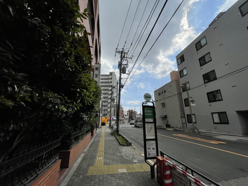 山谷のバス停。左手には緑の植え込みを持つビジネスホテル。