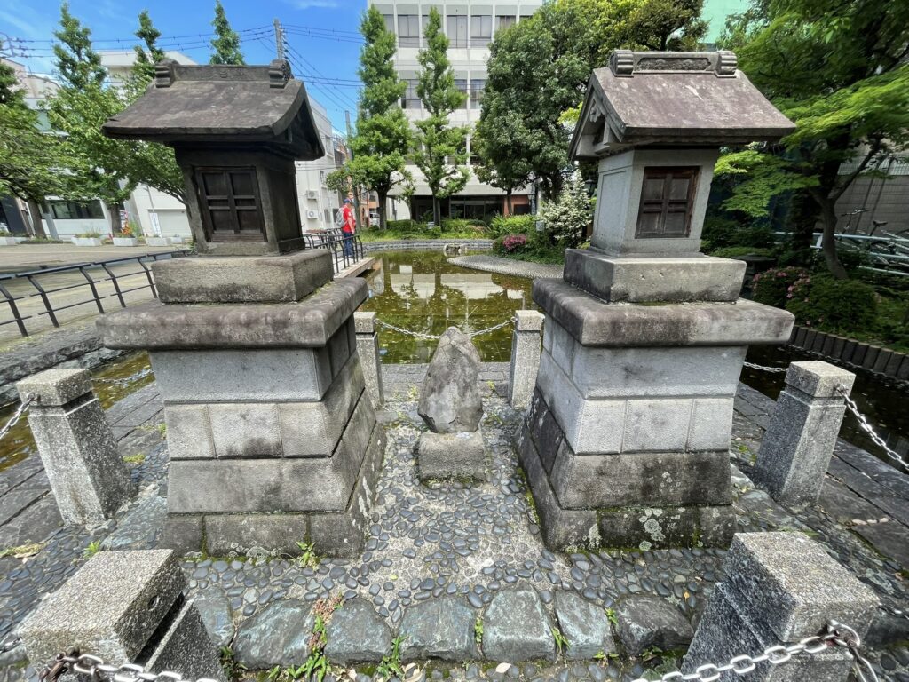 石碑の足元に置かれた小さな石仏と石造物。長い年月を経た風化の跡に、伝説の重み。