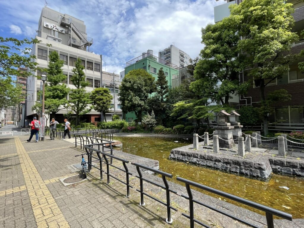 人工池と遊歩道を望む景色。フェンス越しに見える緑と水面が、都市の中にひっそりと残る史跡の静けさを演出している。