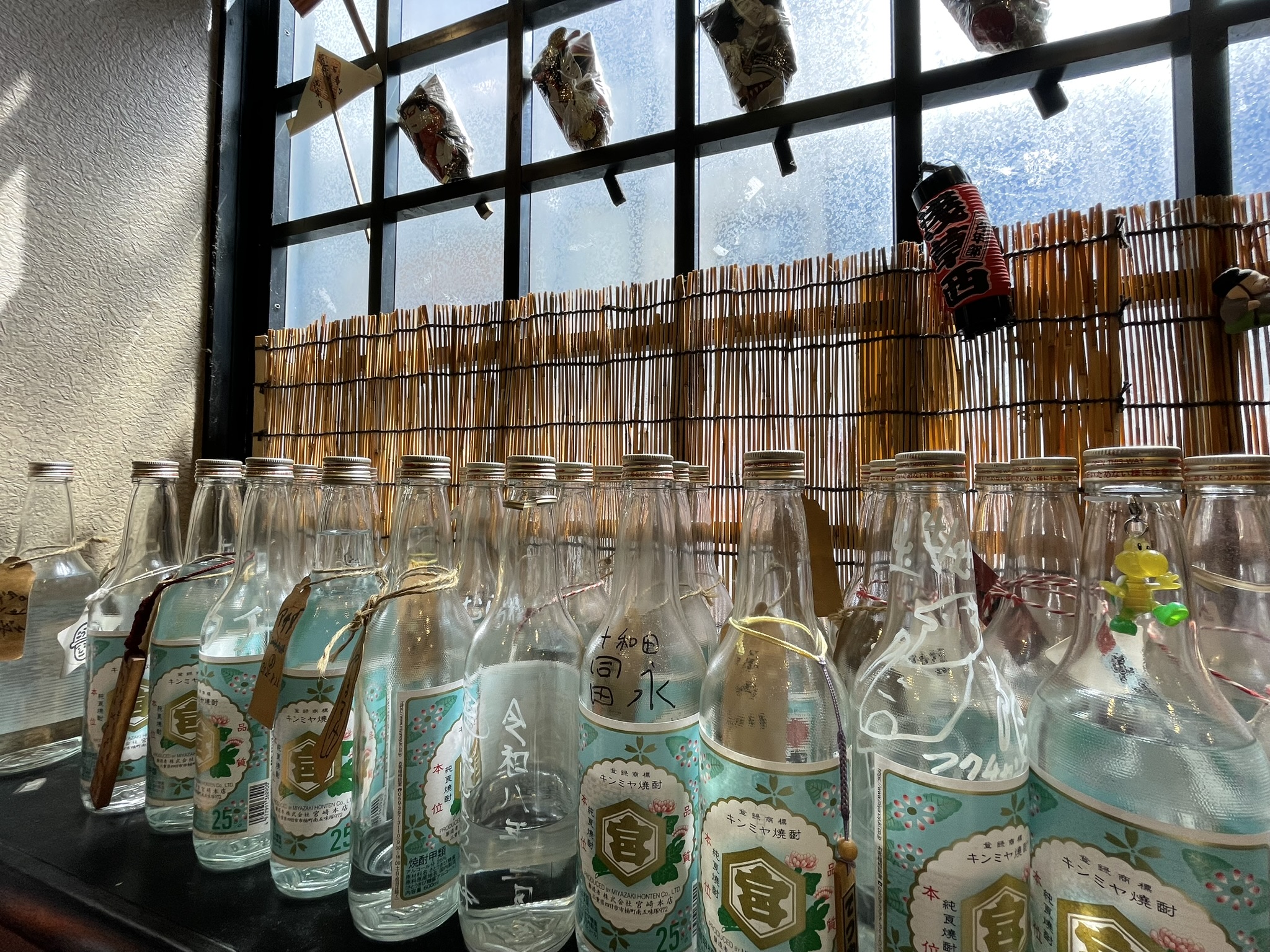 店内の窓際に置かれたボトル。窓には小さな羽子板や提灯が飾られている。