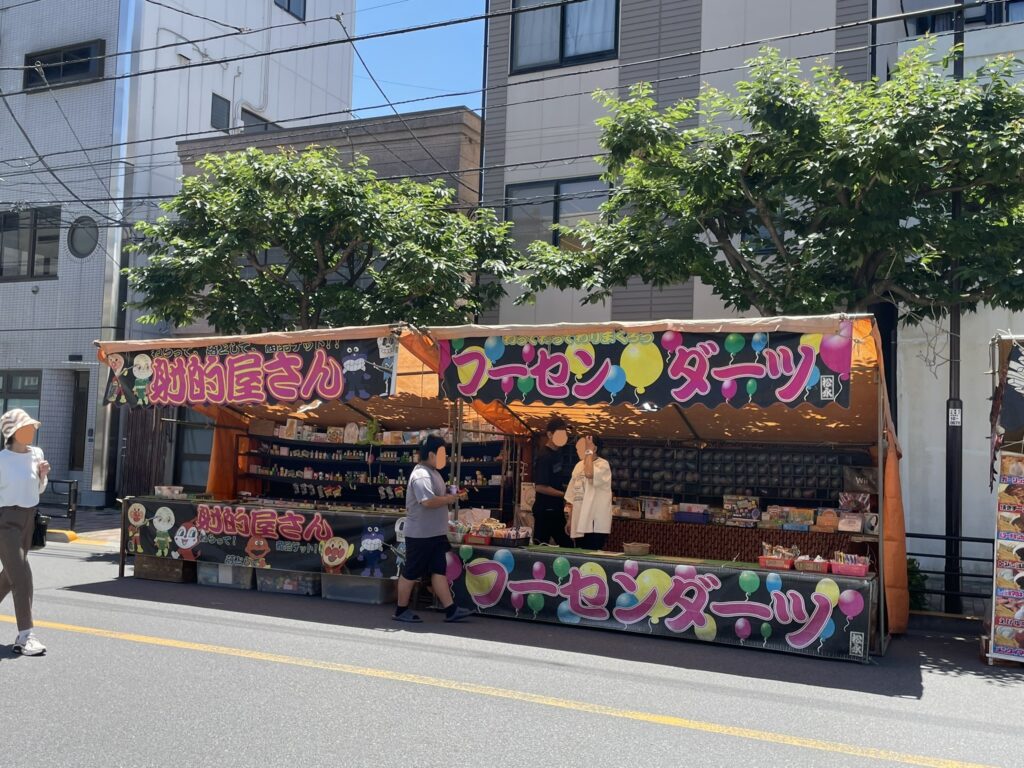 カラフルな看板が目を引く食べ物の屋台。縁日らしい賑やかな雰囲気。