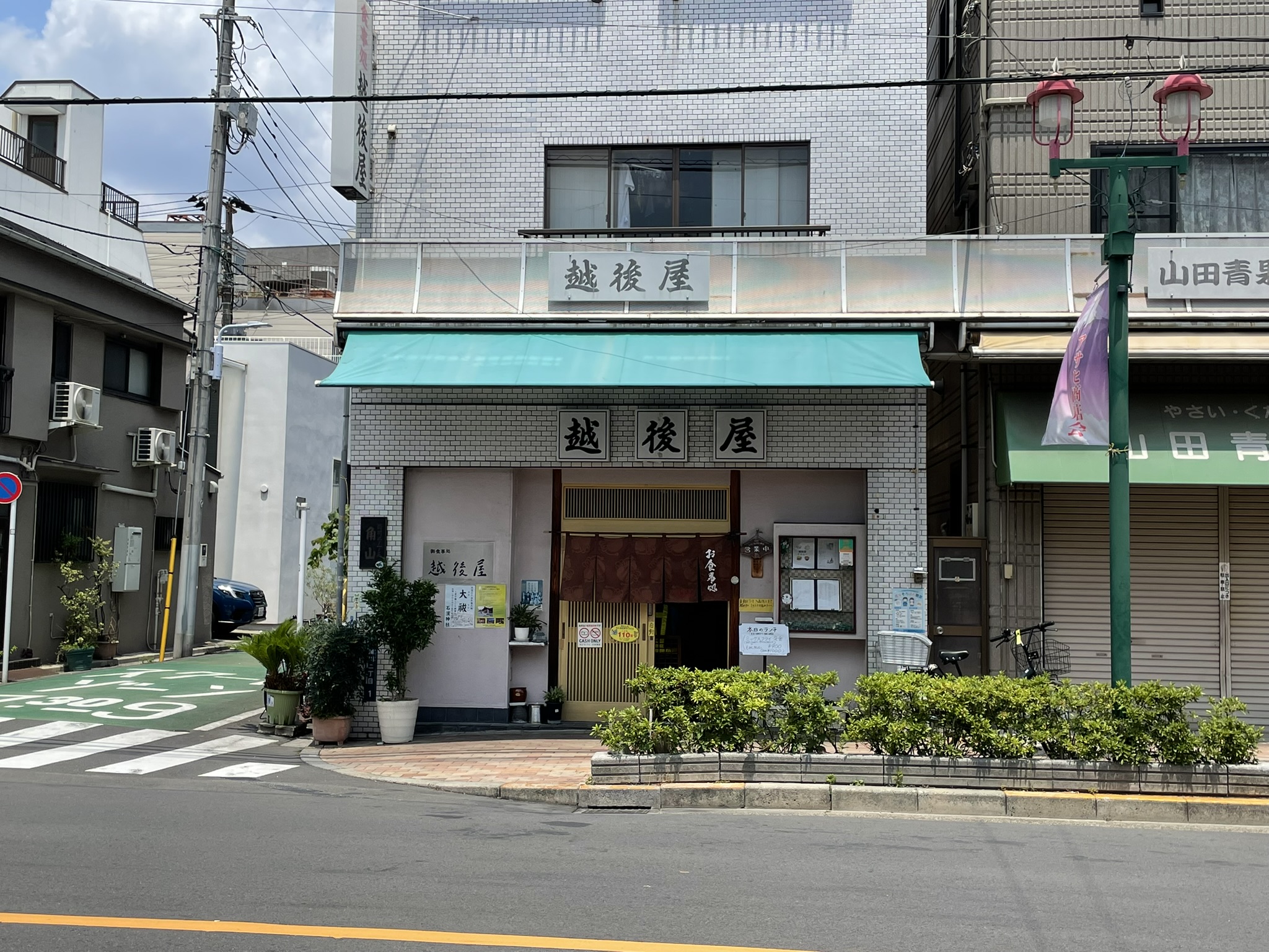 越後屋さんの白いビルの全景。緑色の看板が掲げられている