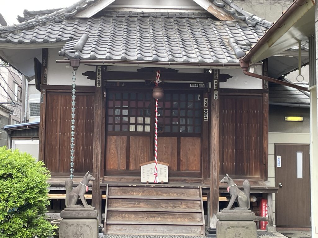 木造のお社の前で、赤い前掛けの狐が守りにつく。