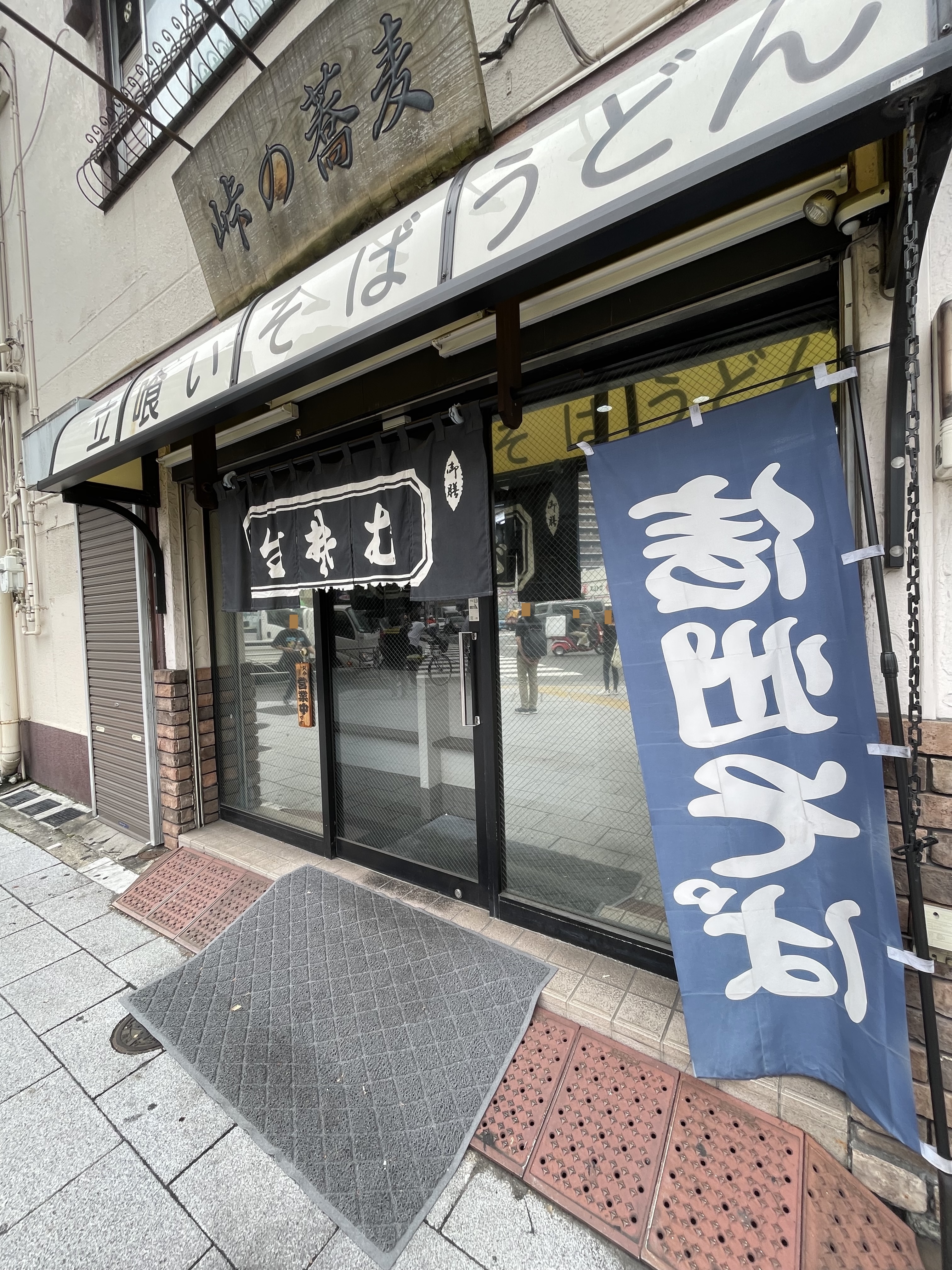 入口にある「生蕎麦」の暖簾（のれん）と「信州そば」の青い幟旗（のぼり）