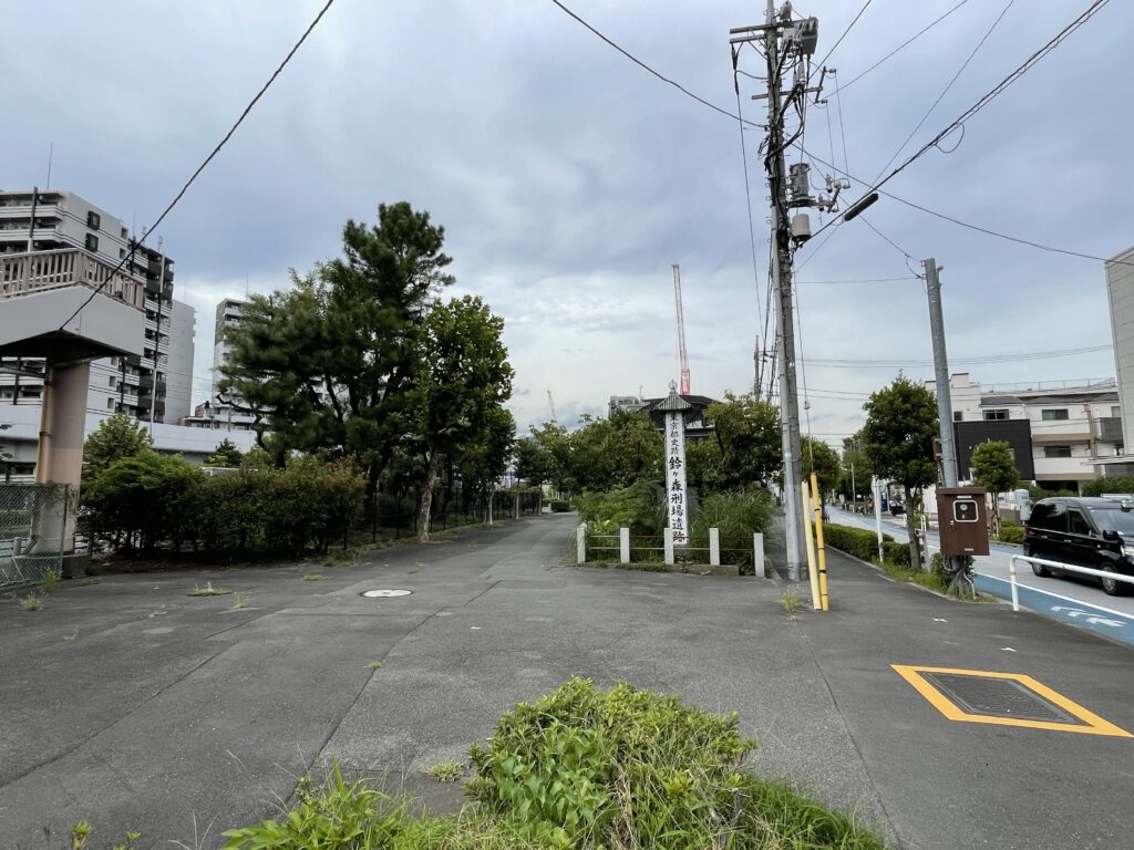 マンションや電柱、国道に囲まれた一角に、屋根付きの標柱がひっそり立っている