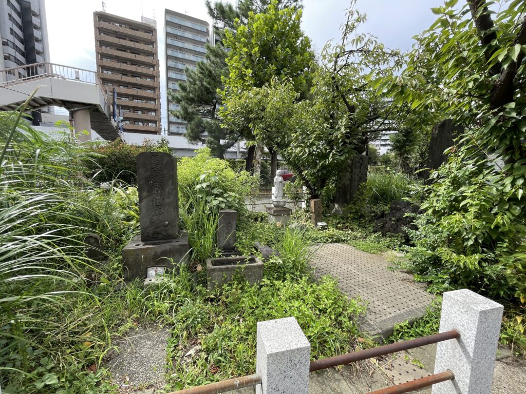 「馬頭観世音」と刻まれた石碑、手水鉢、白い地蔵像が、緑に囲まれて静かにたたずんでいる